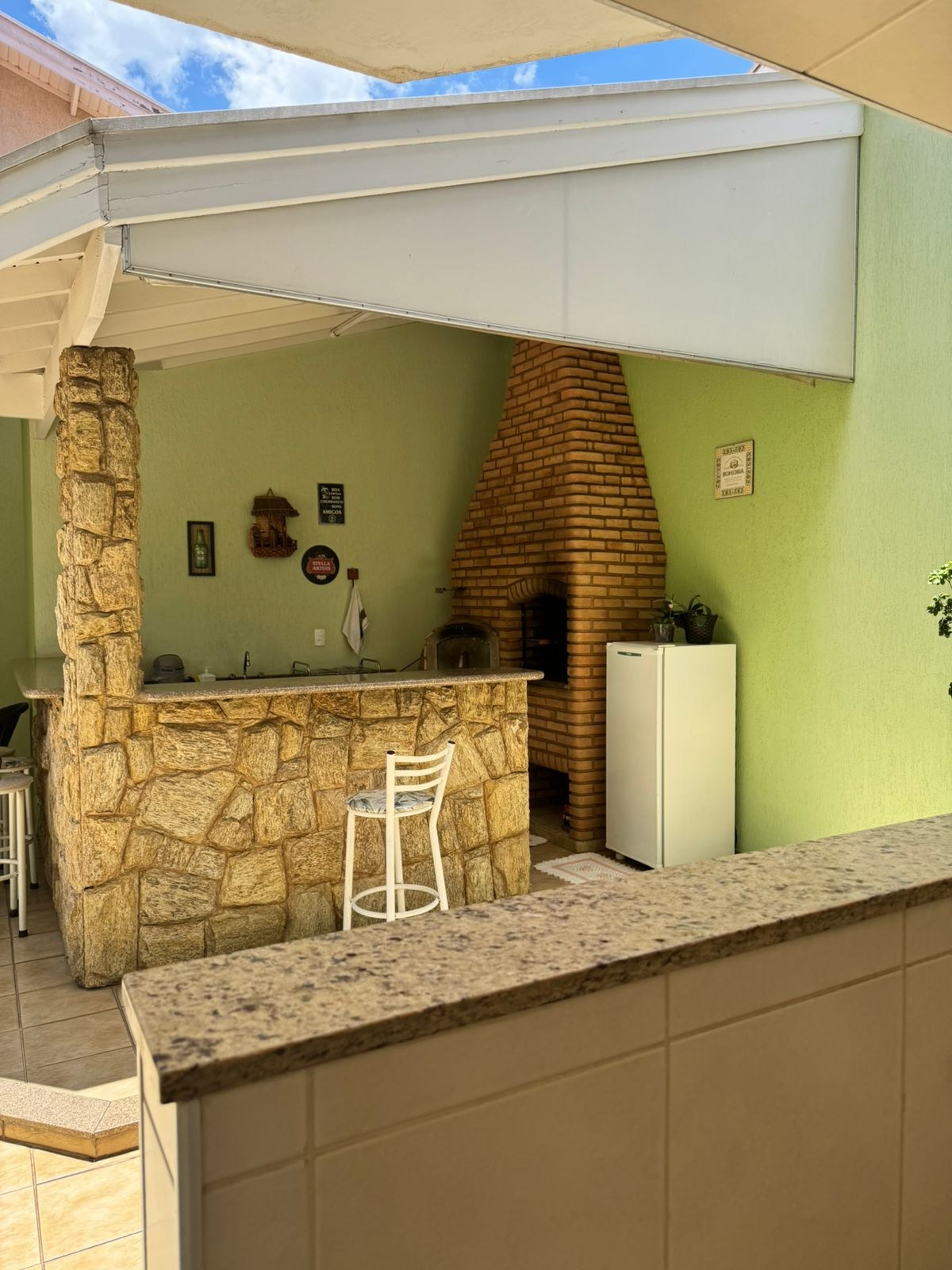 Área gourmet antes da reforma, com bancada revestida de pedra rústica e churrasqueira de tijolo.