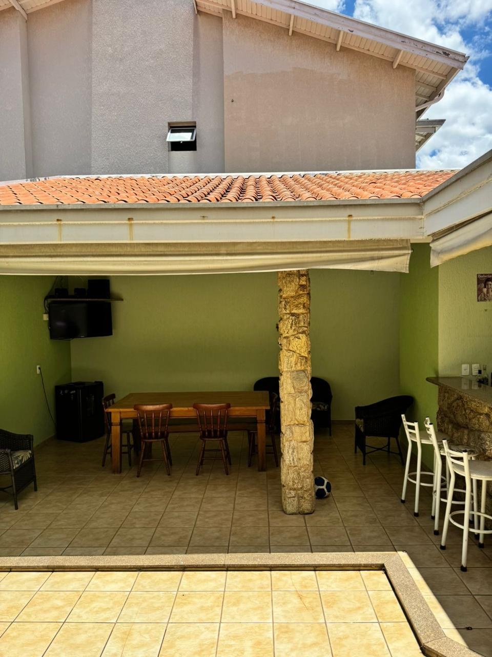 Área gourmet antes da reforma, com parede verde, mesa de madeira e banquetas encostadas na parede.