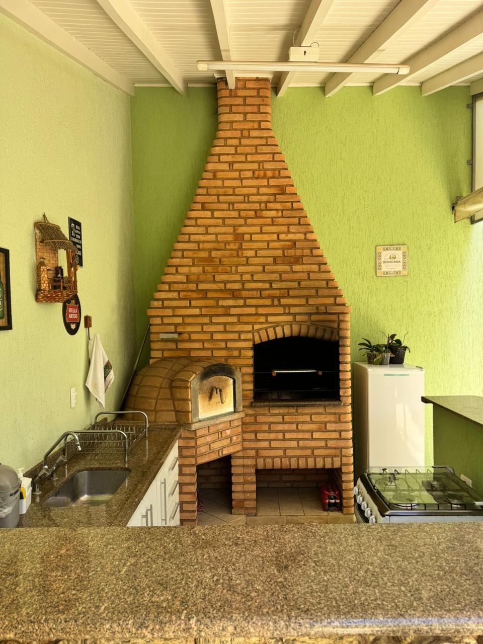 Churrasqueira de tijolo antes da reforma, com parede verde, bancada de granito e pia ao lado.