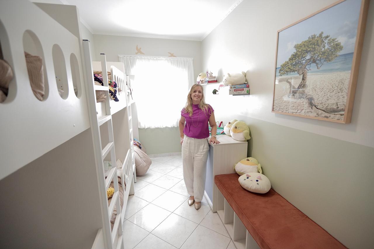 Roberta Pedrotti, designer de interiores, no dormitório infantil projetado por ela, com banco de apoio, almofadas e quadro na parede.