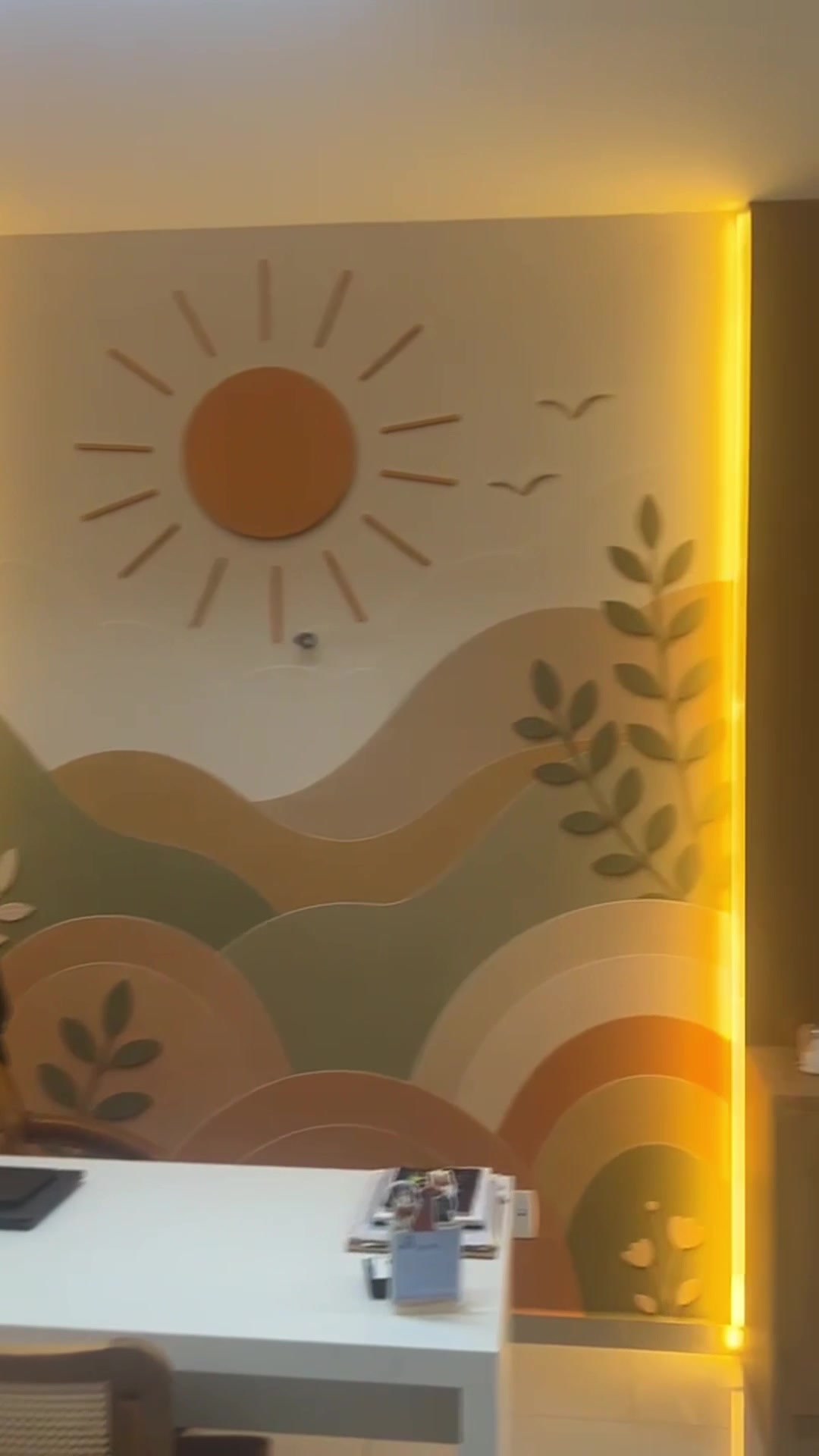 Mural de sol e montanhas em tons de terracota, verde e areia, com fita de LED vertical na quina