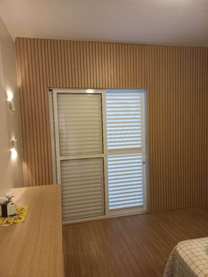 Quarto com parede inteira revestida em ripado de madeira clara, porta-balcão de correr e bancada de madeira no primeiro plano.